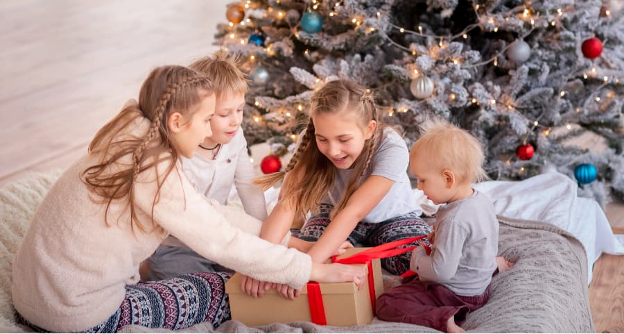 Kids opening a gift in the living room beside a Christmas tree.